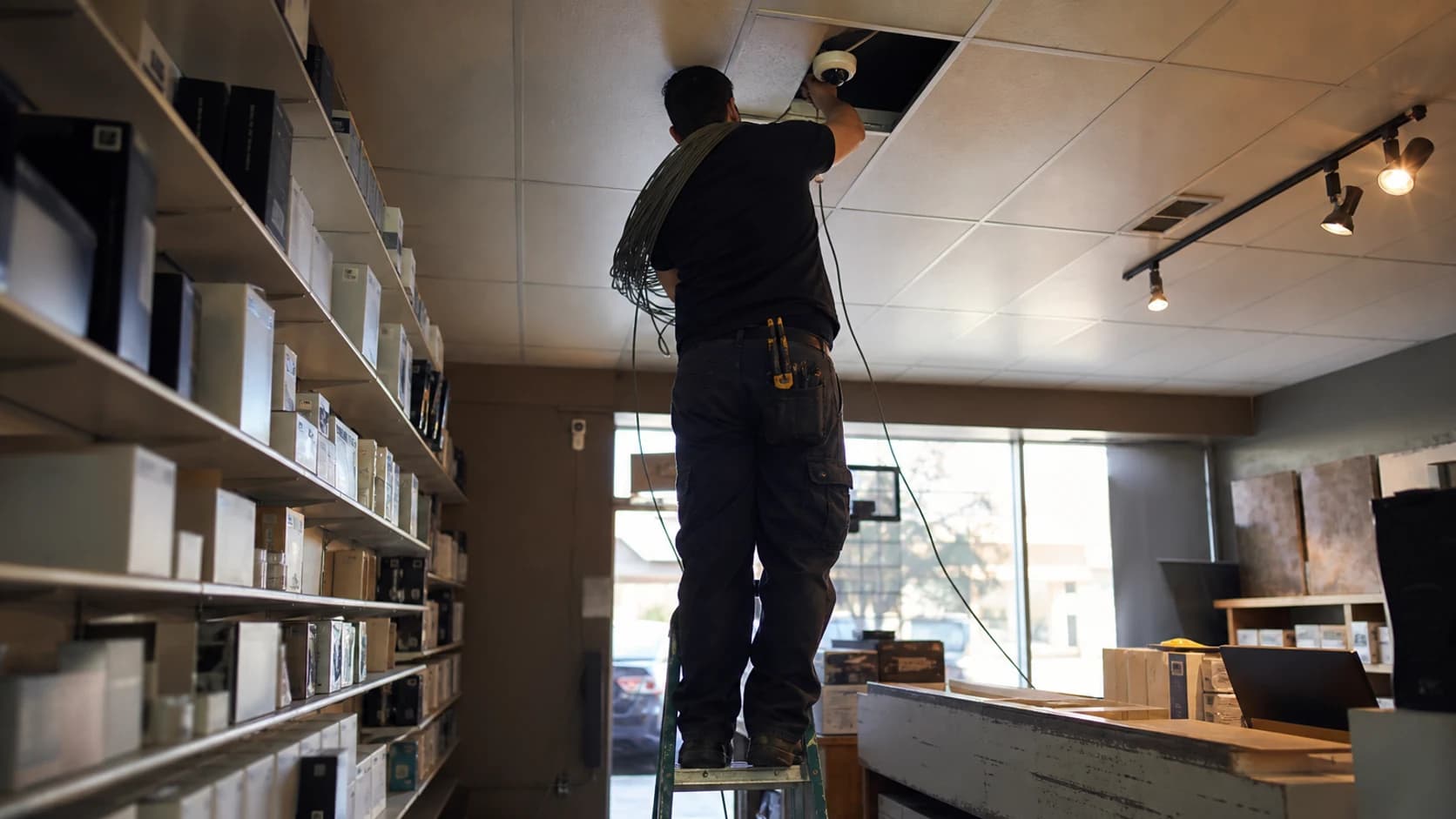 A technician on a step ladder mounting a ceiling camera in a small shop