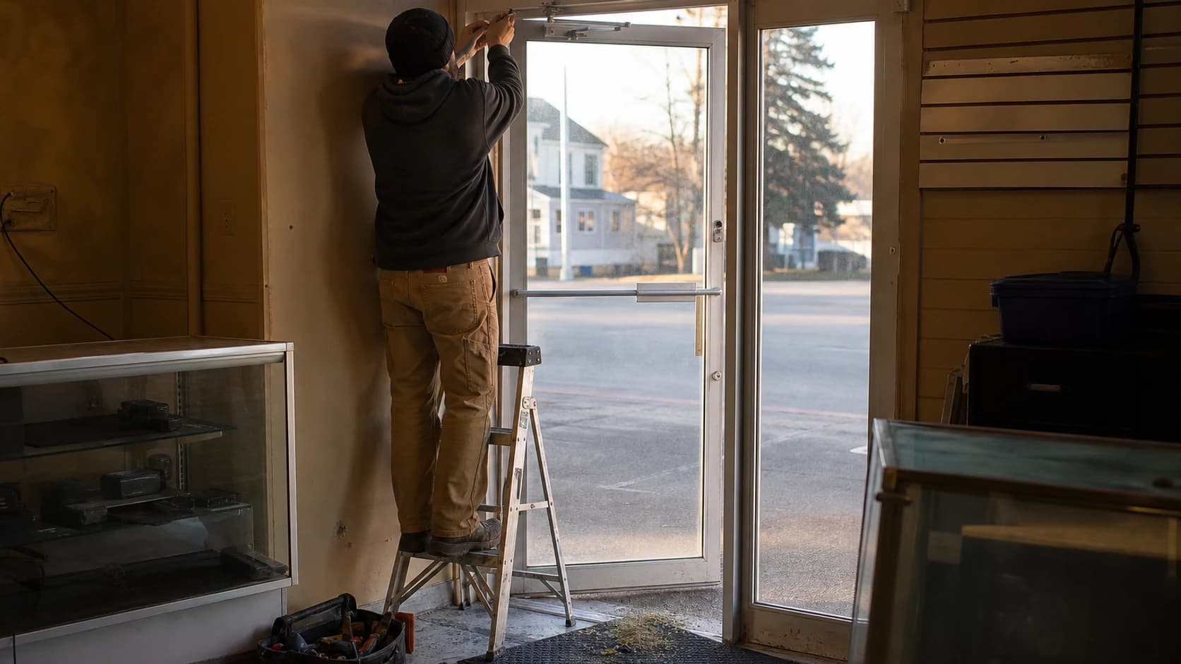 A technician adjusting the overhead closer on a commercial glass entrance door